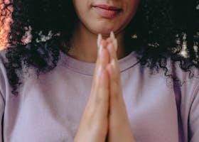 Young woman with curly hair meditating indoors with hands in prayer.